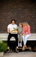 familie met een moeder, vader en dochter zittend buiten Aan de stappen van een voorkant veranda van een steen huis foto