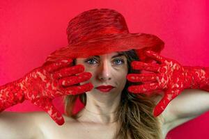 portret van schattig jong vrouw vervelend hoed en rood handschoenen Aan rood achtergrond foto