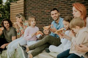 groep van jong mensen en kinderen aan het eten pizza in de huis achtertuin foto