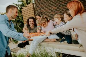 groep van jong mensen en kinderen aan het eten pizza in de huis achtertuin foto