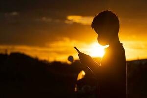 Aziatisch jongen gebruik makend van smartphone Bij zonsondergang foto