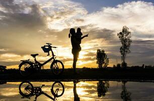 reflectie silhouet van moeder met haar kleuter tegen de zonsondergang. foto