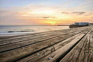 een houten promenade leidend naar de oceaan Bij zonsondergang foto