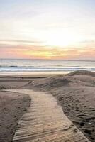 een houten pad Leidt naar de strand Bij zonsondergang foto