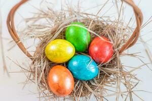veelkleurig Pasen eieren liggen Aan een rietje in de het formulier van een nest in een mand Aan een wit achtergrond. gelukkig Pasen foto