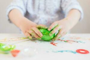 een kind houdt een groen Pasen ei in zijn handen gebrandschilderd met verf Aan een wit tafel. foto