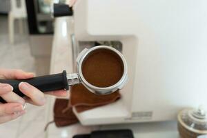de werkwijze van maken koffie stap door stap. Dames aanstampen vers grond koffie bonen in een filterhouder. een koffie brander controle een koffie monster van een koffie brander machine. foto