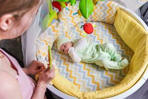 een moeder looks Bij haar pasgeboren baby wie is aan het liegen in een wieg foto