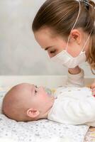 de baby probeert naar scheur uit de beschermend masker van haar moeder s gezicht gedurende de coronovirus en covid-19 pandemie. foto