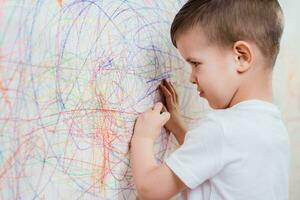 jongen trekt Aan de muur met gekleurde krijt. de kind is verloofd in creativiteit Bij huis foto