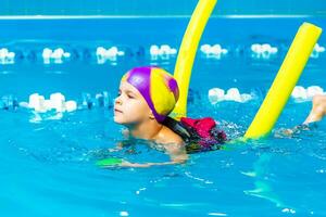 een weinig jongen met een leven jasje Aan zijn borst leert naar zwemmen in een binnen- zwembad. foto