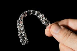 een Mens houdt in zijn hand- transparant aligners plastic een beugel vasthouders voor rechttrekken tanden Aan een zwart achtergrond foto