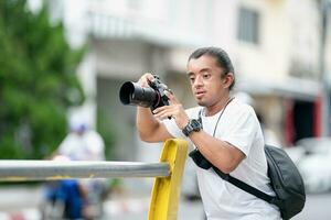 professioneel Aziatisch camera Mens focus Aan de beeld met zijn spiegelloos camera naast de straat buitenshuis veld. foto
