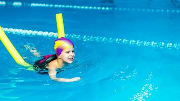 een klein kind met een leven jasje Aan zijn borst is aan het leren naar zwemmen in een binnen- zwembad. foto