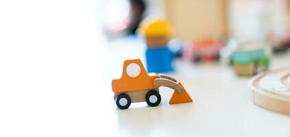 een oranje houten speelgoed- graafmachine is geplaatst Aan de tafel in voorkant van andere wazig houten speelgoed. foto
