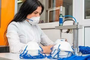 een vrouw werken Bij een machine voor de vervaardiging van medisch maskers met nanovezel en soldeer loops naar hen met echografie. coronovirus en covid-19 het voorkomen foto