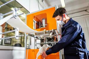 een arbeider staat Bij de machine in een fabriek voor de vervaardiging van medisch maskers met nanovezel. coronovirus en covid-19 bescherming foto