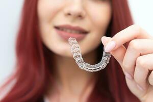 een vrouw met een mooi glimlach houdt aligners in haar hand- foto