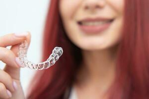 een vrouw met een mooi glimlach houdt aligners in haar hand- foto