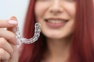 een vrouw met een mooi glimlach houdt aligners in haar hand- foto