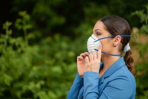 mooi meisje zet een medisch masker Aan haar gezicht Aan de natuur. coronavirus en covid-19 bescherming foto