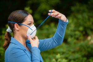 mooi meisje zet een medisch masker Aan haar gezicht Aan de natuur. coronavirus en covid-19 bescherming foto