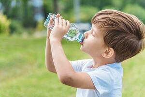 schattig kind drankjes water van een fles Aan de straat in zomer foto