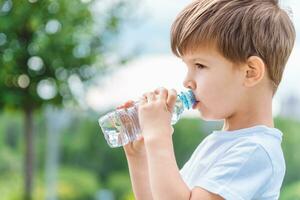 schattig kind drankjes water van een fles Aan de straat in zomer foto