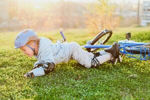 een klein kind in een helm en bescherming viel van een fiets op de gras en was niet gewond foto