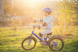 weinig jongen in helm ritten een fiets Aan een zonnig dag foto