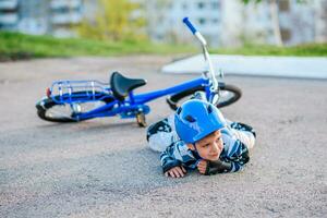 een weinig jongen in een helm viel van een fiets op de asfalt en was niet gewond foto