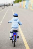 een kind in een helm en bescherming in een fiets rijden Aan natuur in de voorjaar foto