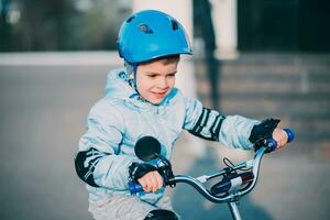 weinig jongen in helm ritten een fiets Aan een zonnig dag foto