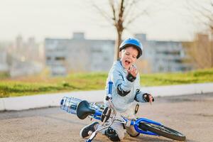 een weinig jongen in een helm viel van een fiets op de asfalt en was niet gewond foto