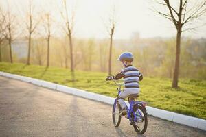 een kind in een helm en bescherming in een fiets rijden Aan natuur in de voorjaar foto