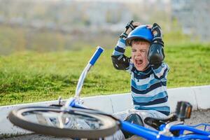 een klein kind viel van een fiets op de weg, huilen en schreeuwen in pijn. foto