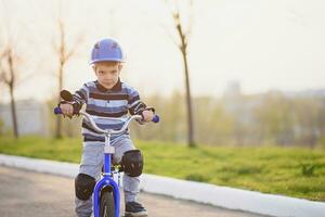 een kind in een helm en bescherming in een fiets rijden Aan natuur in de voorjaar foto