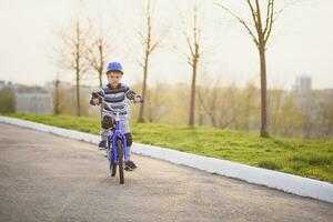 een kind in een helm en bescherming in een fiets rijden Aan natuur in de voorjaar foto