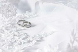 twee klassiek bruiloft ringen in wit goud tegen een wit kralen en parel bruids sluier. een kopiëren van de ruimte. selectief focus. foto