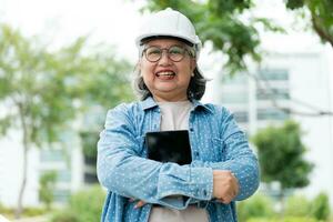 gelukkig ouderen Aziatisch professioneel ingenieur draagt een helm en cheques de blauwdruk Aan een tablet Aan de bouw plaats na de aannemer en architect af hebben vernieuwing de huis en gebouw foto