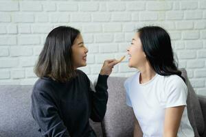 gelukkig lesbienne paar aan het eten snacks samen Aan de sofa Bij huis, ontspanning. foto