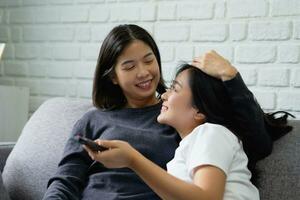 gelukkig Aziatisch lesbienne gebruik makend van afgelegen controle aan het kijken TV Bij huis, moment uitgeven mooi zo tijd samen foto