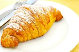 een stuk van croissant brood in een wit bord Aan de tafel. foto