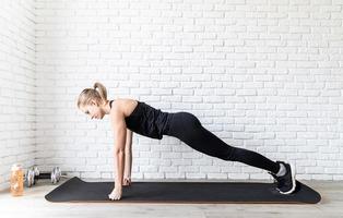vrouw in zwarte sportkleding die thuis push-ups doet foto