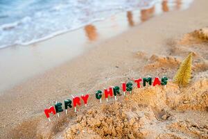vakantie door de zee. viering van de traditioneel december vakantie in de buurt de oceaan. de tekst van een vrolijk Kerstmis gemaakt van kaarsen De volgende naar de schuimend Golf. foto