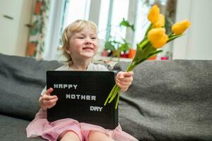 weinig meisje houdt een boeket van geel tulpen en een teken dat zegt gelukkig moeder dag. kind geeft bloemen naar moeder voor vakantie. foto