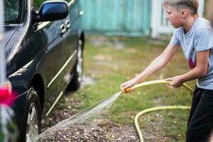 kind het wassen auto wielen met water van een tuin slang in de achtertuin van de huis foto