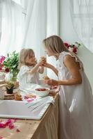 een weinig blond meisje met haar mam Aan een keuken aanrecht versierd met pioenrozen. de concept van de verhouding tussen moeder en dochter. voorjaar atmosfeer. foto