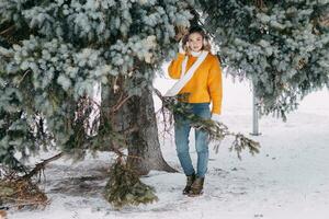 tiener blond in een geel trui buiten in winter. een tiener- meisje Aan een wandelen in winter kleren in een besneeuwd Woud foto