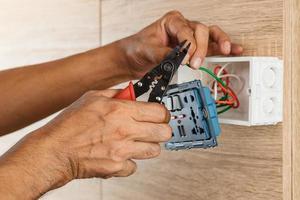 elektricien stript elektrische draden in een plastic doos op een houten muur om het stopcontact te installeren. foto